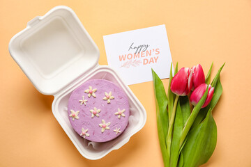 Plastic lunch box with tasty bento cake, greeting card and flowers for International Women's Day celebration on orange background