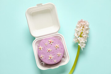 Obraz na płótnie Canvas Plastic lunch box with tasty bento cake and flowers for International Women's Day celebration on turquoise background