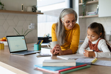 Small girl with senior grandmother doing homework at home.