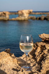 Glass of cold white dry white wine served on rocks in blue sea bay near Protaras touristic town on Cyprus