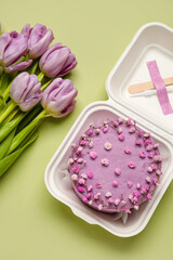 Plastic lunch box with tasty bento cake and flowers on green background