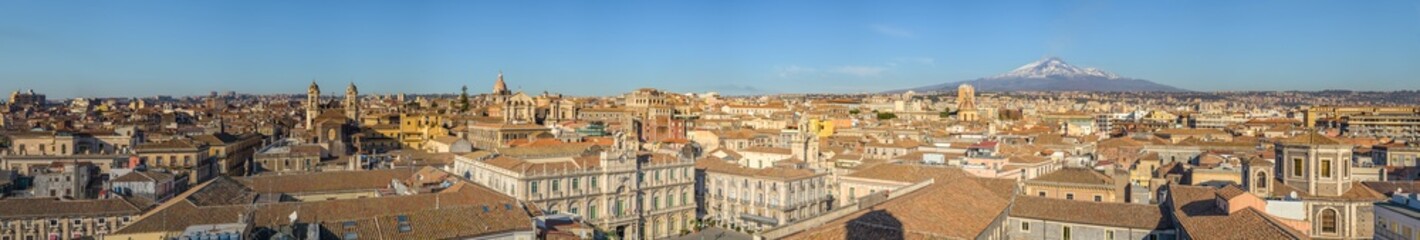 Banner panorama of Catania city center from Saint Agatha church terrace, with historic buildings, churches and university, and Mount Etna volcano erupting in Sicily, Italy