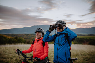 Senior couple bikers with binoculars admiring nature outdoors in meadow in autumn day.