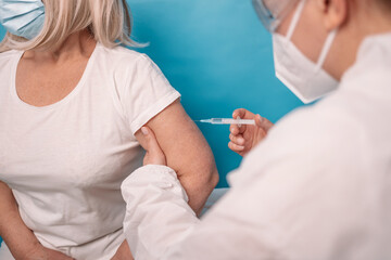 Vaccinating an elderly person. Doctor makes vaccination to senior woman, wearing face mask over blue background.