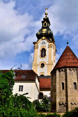 Fototapeta premium Im Vordergrund rechts der Karner (Gebeinshaus) und im Hintergrund der Kirchturm der Stadtparrkirche in Hartberg in der Oststeiermark