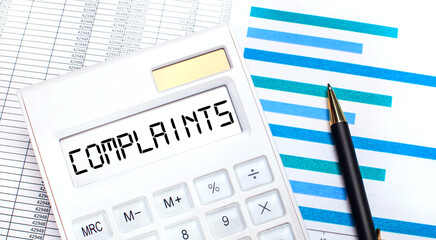 Against the background of reports and blue graphs, a pen, and a white calculator with text on the COMPLAINTS screen. Business concept