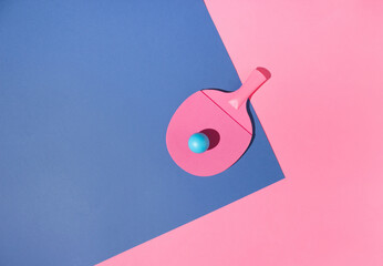 A pink table tennis racket with a blue tennis ball on a blue and a pink background. Minimal concept.