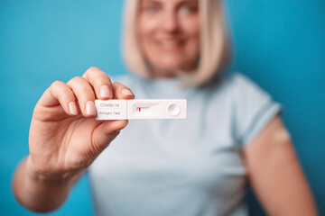 Vaccinated woman holding an antigen test with negative result for COVID-19 pandemic, showing arm with plaster over bright blue color background