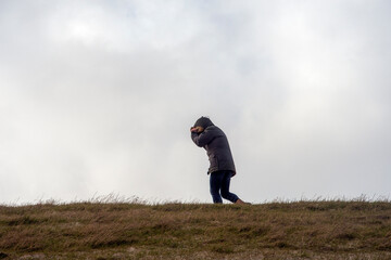 A man walks against the storm and protects his face from the strong wind