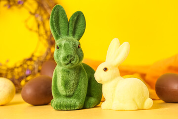 Cute Easter bunnies and chocolate eggs on yellow background