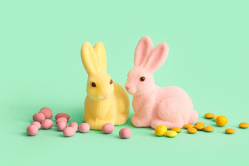 Easter bunnies and candies on color background