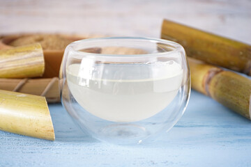 Fresh cane juice and sugarcane on a wooden background, closeup.
