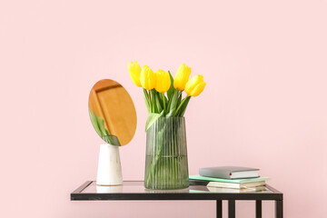 Vase with tulips, mirror and notebooks on table near color wall