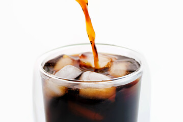 Black coffee is poured into a glass with ice close up on white background.