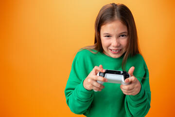 Young pretty teen girl playing with console joystick over orange background