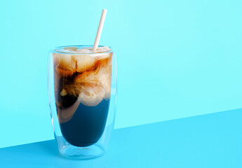 Coffee with milk and ice in glass cup on blue background, copy space.
