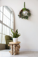 Beautiful Easter wreath, table with houseplant and mirror near white wall