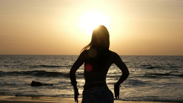 Spectacular silhouette of a woman performing belly dance on the beach with the sunset.