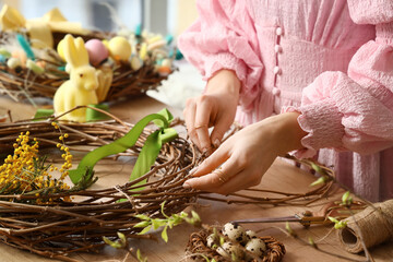 Obraz na płótnie Canvas Woman making beautiful Easter wreath on wooden table, closeup