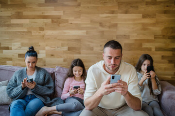 Family with two little daughters, everyone is using mobile phone in the living room.