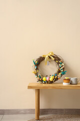 Delicious cake, cups and Easter wreath on wooden bench near color wall