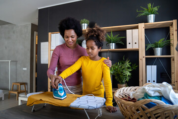 Fototapeta premium Beautiful young woman and child girl little helper are having fun and smiling while ironing at home.