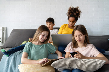 Group of multiethnic teenagers with modern gadgets and laptop having fun, studying together at home