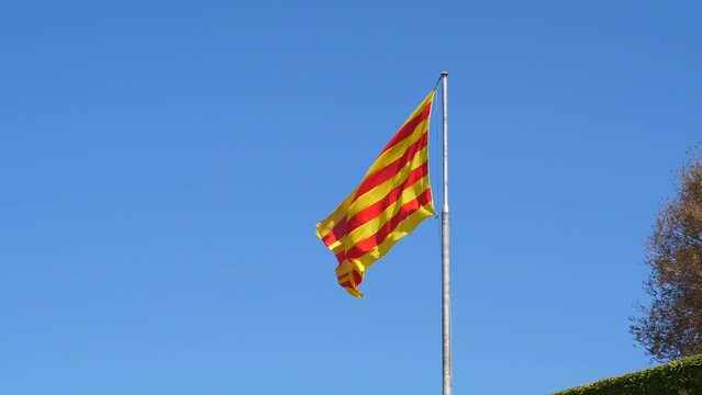 Four red stripes on yellow field, flag wave in air, super slow motion shot. Senyera standard, flag of Catalonia, Aragon, Balearic Islands, Valencia at top of Montjuic Castle in Barcelona
