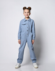 pretty girl with bagel hairdo standing straight in blue cotton summer jumpsuit with comfortable pockets. on a light background. Children's fashion