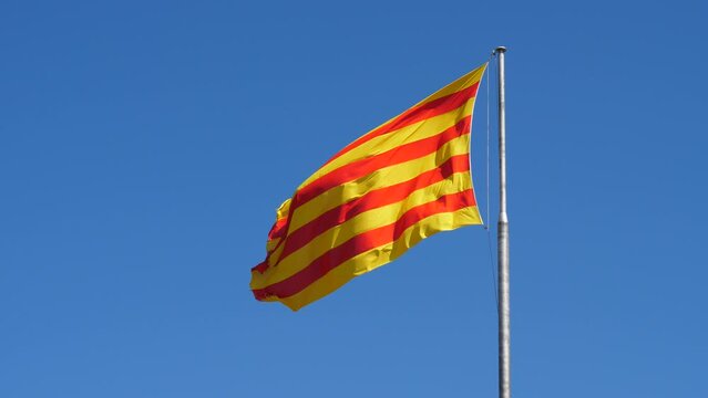 Large Senyera flag wave on wind against clear blue sky. Vivid colours of standard in daylight, four red stripes on yellow field. Shoot at Barcelona, Spain