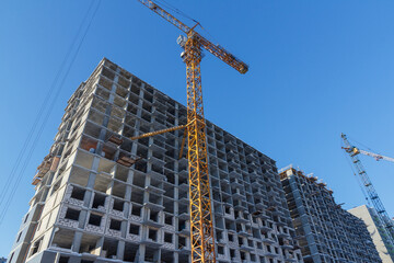 Residential building construction. Crane and building construction site against blue sky.