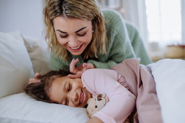 Happy mother stroking her little daughter when waking her up in morning. - obrazy, fototapety, plakaty