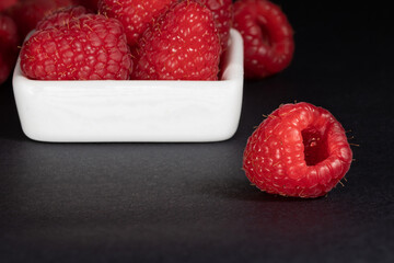 Raspberries in a white saucer on a black background