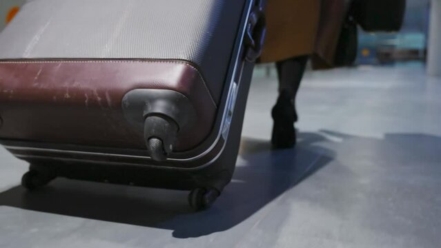 Back view of female legs and suitcase, woman the runs with a suitcase, hurrying to her flight and rolling bag near, close up