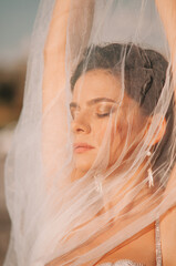Close-up portrait of a brunette model girl in the role of a bride. Beautiful face, portrait at sunset in summer day.