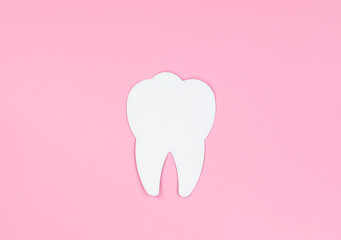 Dental care concept, copy space. White tooth on a pink background.