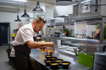 Chef decorating soups in takeaway bowls indoors in restaurant kitchen.
