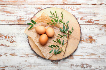 Board with Easter eggs and leaves on light wooden background