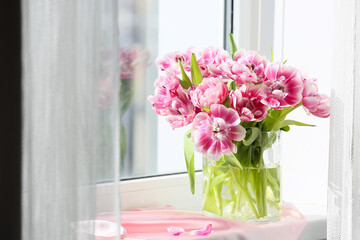 Glass vase of beautiful tulips on windowsill