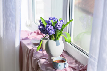 Vase with blooming hyacinths, cup of tea and candles on windowsill