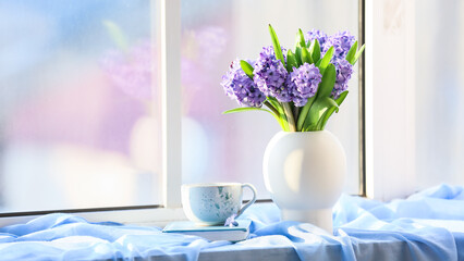 Vase with beautiful blooming hyacinths, book and cup of tea on windowsill