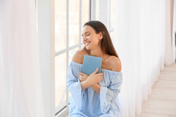 Pretty young woman with book near window