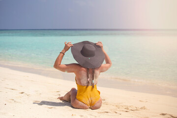 Young woman back view unrecognized wearing hat and swimming suite on the tropical beach, Maldives