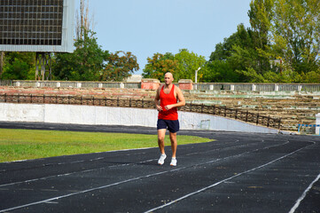 Obraz premium young male athlete in a red jersey conducts a running training at the stadium. man running on black rubber track outdoors
