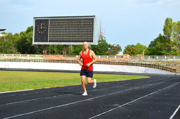Obraz premium young male athlete in a red jersey conducts a running training at the stadium. man running on black rubber track outdoors