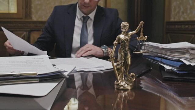 Midsection shot of male lawyer stamping documents at office table with Themis statue on it
