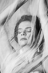 Black and white portrait of a beautiful girl in a dress with a veil close-up. The wind develops hair and fabric. Concept - fashion photography