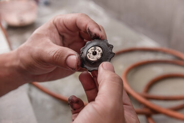 A repairman or technician inspects a derailleur pulley cog of a mountain bike prior to cleaning. Maintenance service at a bicycle repair shop. - obrazy, fototapety, plakaty