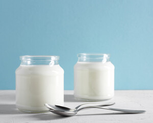 Yogurt, kefir or fermented milk product in glass jars on a white table. White and blue background. Healthy food concept