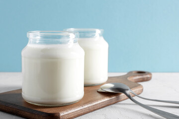 Yogurt, kefir or fermented milk product in glass jars on a wooden board. Healthy food concept. White and blue background